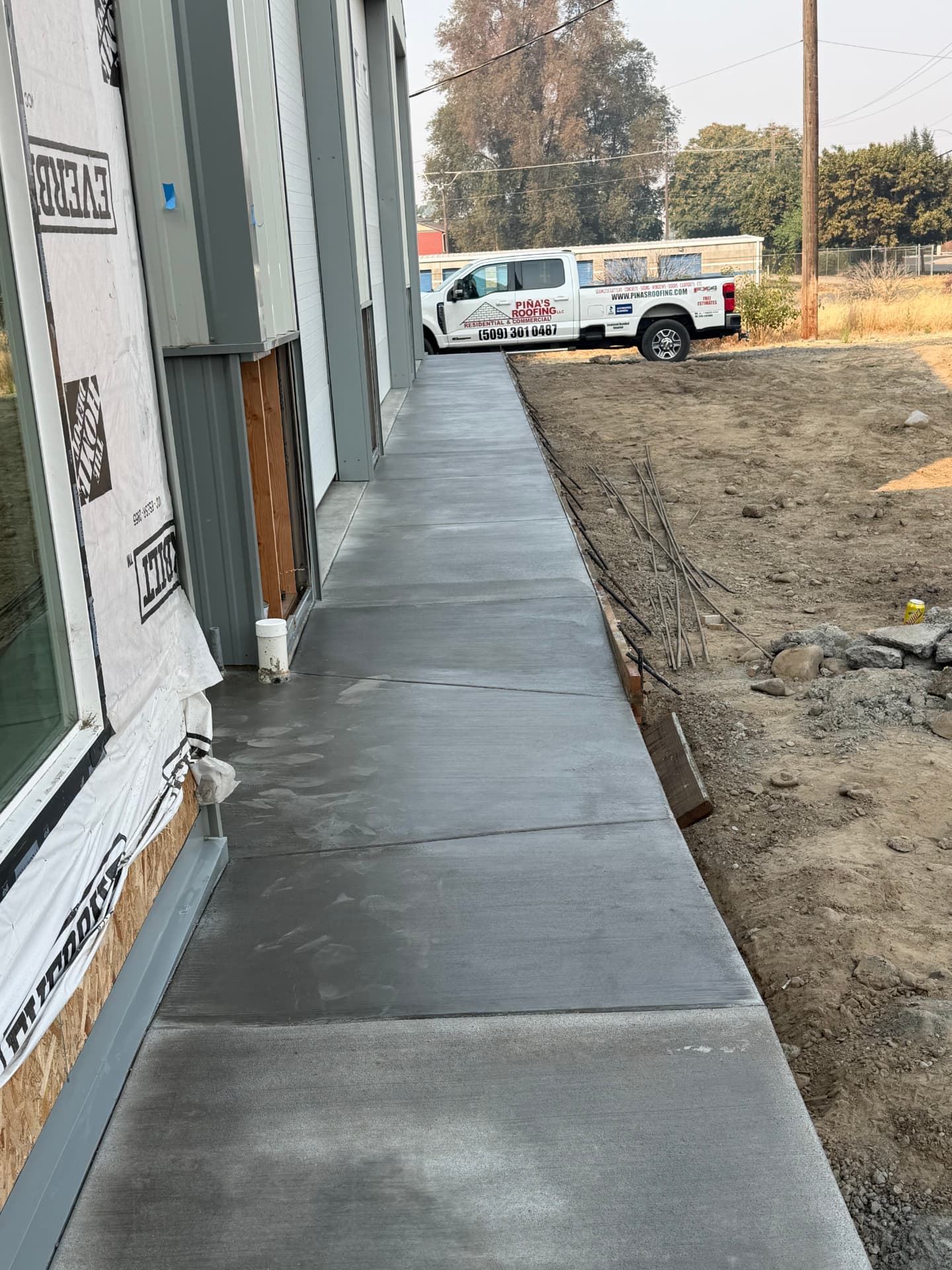 Completed smooth concrete walkway alongside a commercial building with a Piña's Roofing truck parked nearby